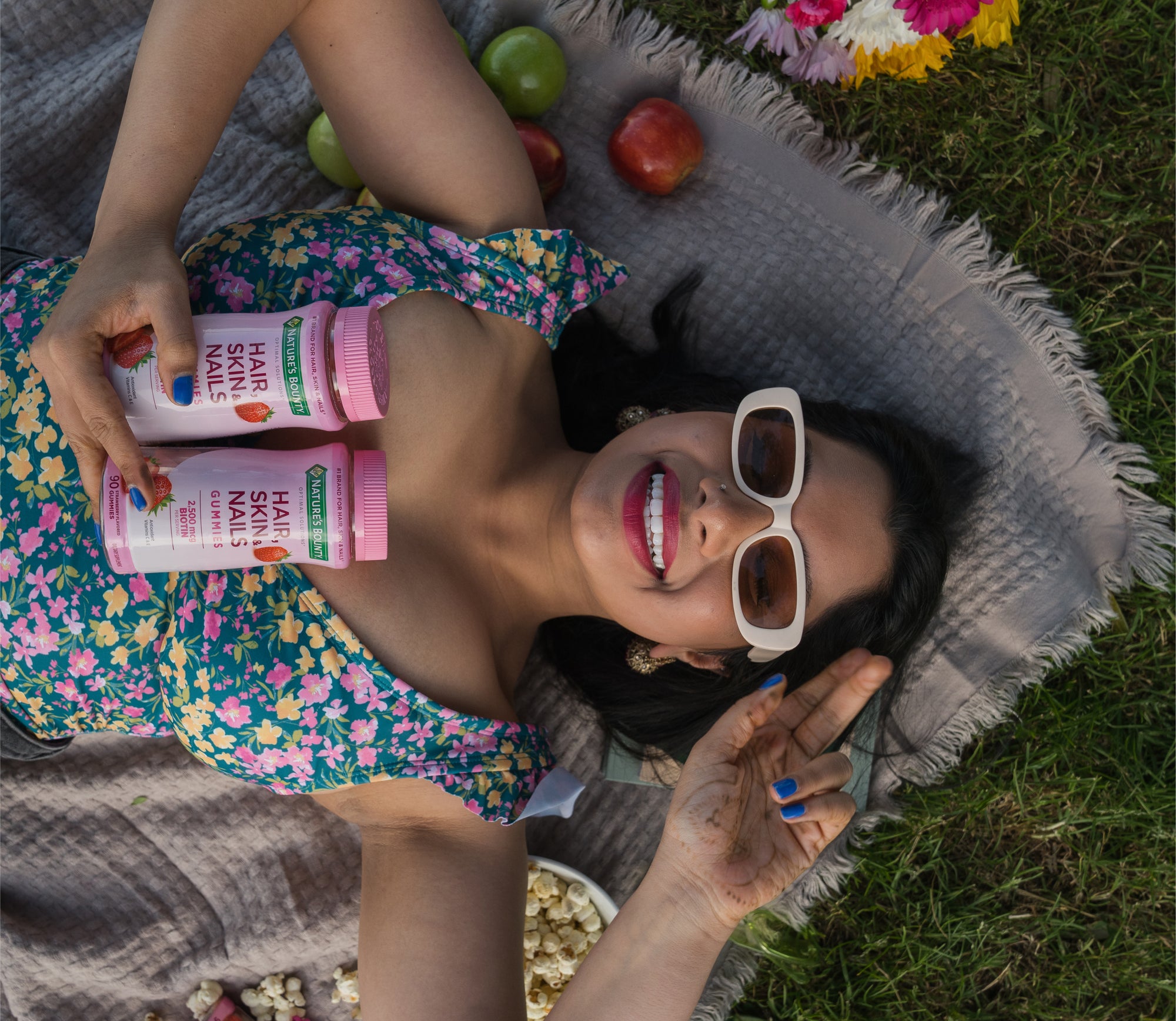 Woman laying on blanket in grass holds Nature's Bounty® Hair Skin Nails product